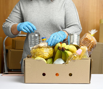 妇女戴手套时不断收集食物水果和品并用纸板盒帮助有需要的人帮助和志愿的概念图片