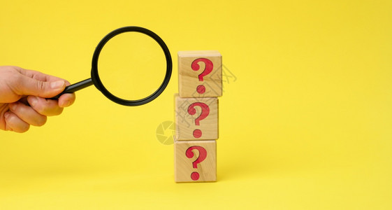 带有问号的木制立方块和女手在黄色背景上有一个放大镜寻找未知问题的答案解决问题的概念查找信息图片