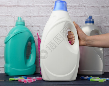 妇女手拿着一个大白塑料瓶用洗涤剂衣服与白砖墙背景相对图片