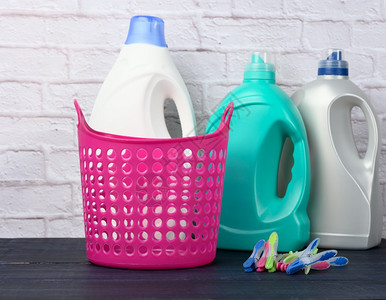 白色砖墙背景上的空粉红色洗衣篮和装有液体洗涤剂的塑料瓶图片