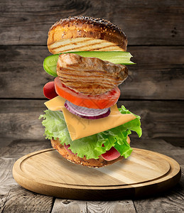 起司汉堡芝士麻面包炸牛排绿色沙拉和番茄片圆木板上的三明治图片