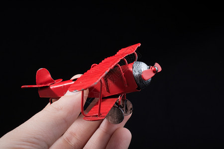 在黑色背景上手持红色玩具飞机图片