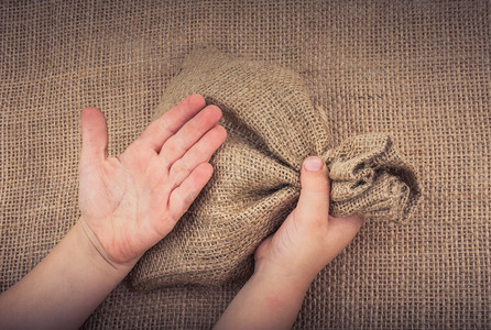 手握着用亚麻布制成的空小麻袋背景