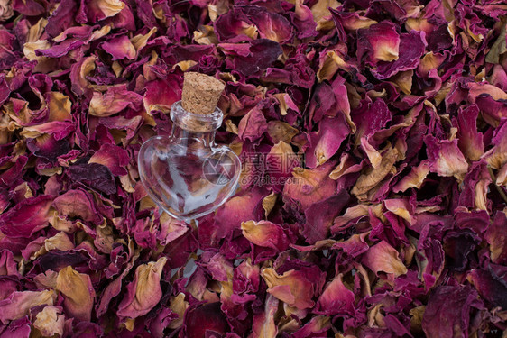 以干玫瑰花瓣背景的心形瓶子图片
