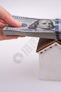 手持美元钞票在白色背景的模范房屋顶上图片