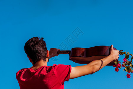 年轻人在蓝天上举起一把音乐吉他图片
