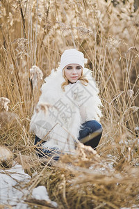 穿着白色毛皮夹克和帽子的女孩在冬天草丛中美丽金发女郎在冬天站9147号后床里图片