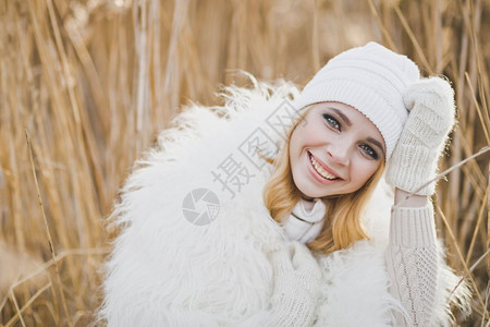 穿着白色毛皮夹克和帽子的女孩在冬天草丛中美丽金发女郎在冬天站914号后床里图片