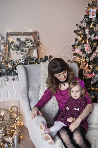 婴儿和母亲坐在圣诞树附近的椅子上女儿和母亲坐在圣诞树附近的椅子上图片