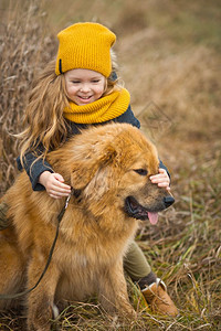 穿着黄帽子和围巾的小女孩打着一只大红狗的脸背景图片