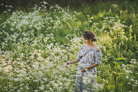 一位孕妇站在开满花的草原上图片