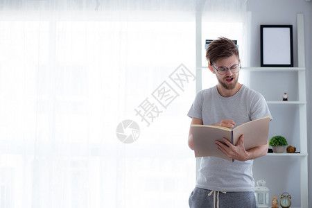 戴眼镜的帅哥正在读书准备考试和思站在起居室教育概念背景图片