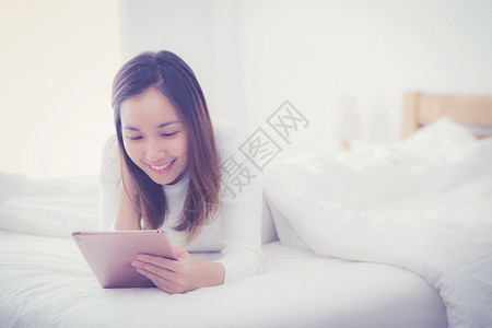 睡在卧室里的女人睡在早晨的阳光下用数字平板手指触摸图片