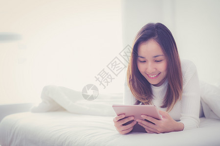 睡在卧室里的女人睡在早晨的阳光下用数字平板手指触摸图片