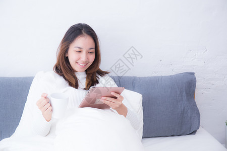 睡在卧室的亚洲女人带着数字片子喝咖啡在早晨的生活方式概念图片