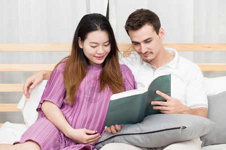 年轻孕妇和丈夫在沙发上看书图片