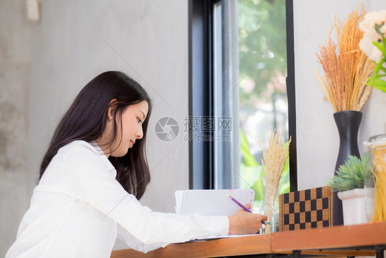 美丽的商业女青年在桌子上的笔记本写作女孩在咖啡店工作自由职业概念图片