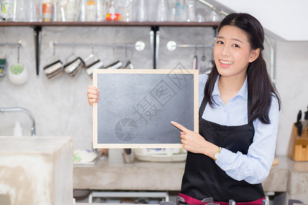 美丽的年轻咖啡师肖像女是一名员工站在柜台咖啡店的黑板上服务概念图片