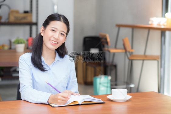 美丽的商业女青年在桌子上的笔记本写作女孩在咖啡店工作自由职业概念图片