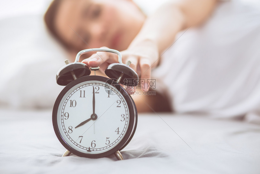 美丽的亚洲年轻女在清晨关闭闹钟醒来睡觉时