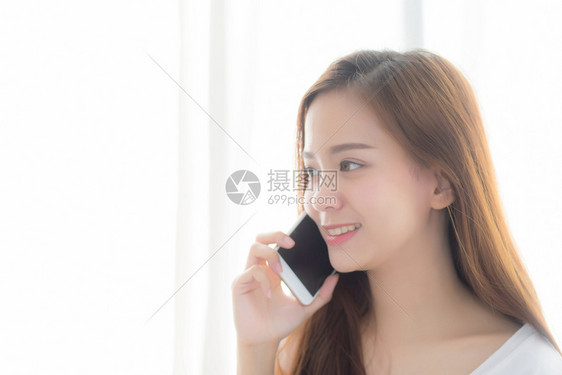 美丽的肖像年轻亚洲女说智能手机微笑站在窗帘背景卧室女孩呼叫电话通信概念图片