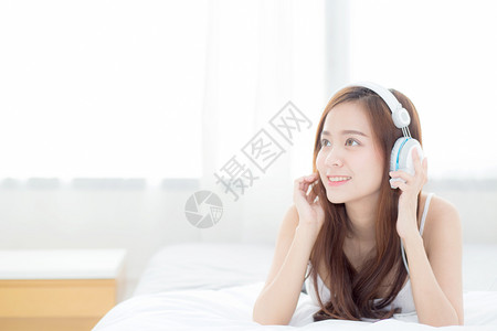 美丽的亚洲年轻女在睡房时享受耳机听音乐放松女孩在网络上听耳机闲暇与科技概念背景图片