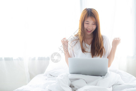 使用笔记本电脑工作的年轻美丽快乐青女在家中的床上工作成功图片