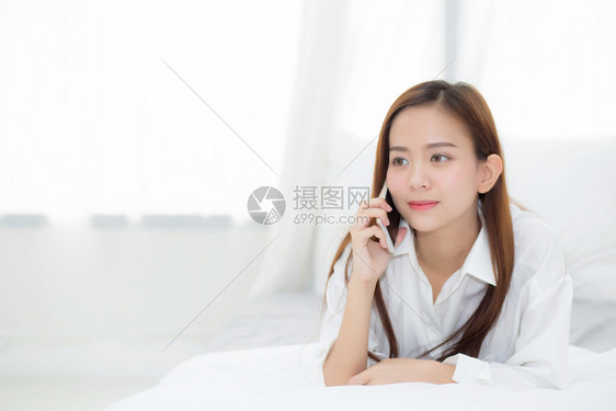 美丽的年轻女早上在床微笑着躺放松女孩使用移动智能电话聊天交流概念图片