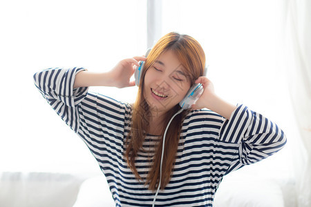 美丽的亚洲年轻妇女享受和听音乐的趣耳机坐在卧室女孩用耳机闲暇和技术概念放松图片