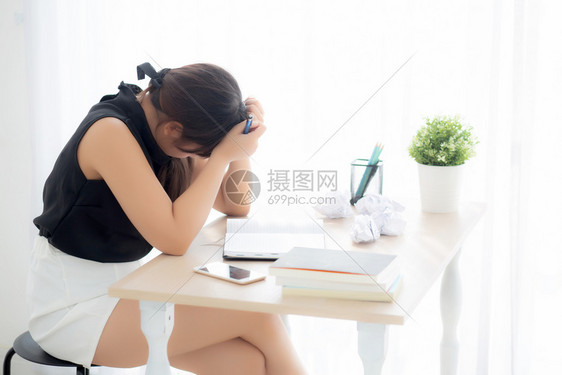 美丽的亚洲妇女疲惫不堪在办公桌上写作过量压力重女孩对办公室的笔记本和折叠纸自由职业者和商概念一无所顾虑图片