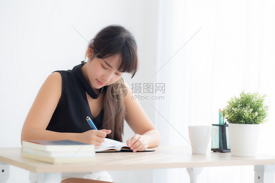 美丽的年轻女士在家中客厅里微笑地坐着学习写笔记本和日做女孩功课在桌子上工作的商业妇女教育概念图片