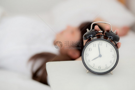 美丽的亚洲年轻女在早上关闭闹钟醒来后用放松和生活方式概念睡觉图片