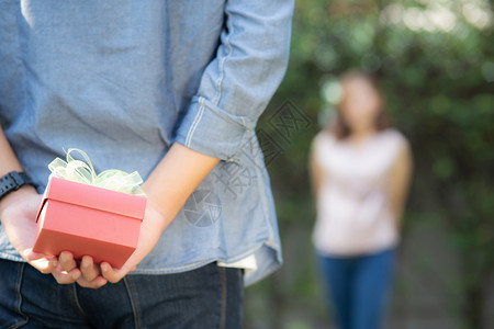 年轻的亚洲男人背着礼物盒拿惊喜的女朋友兴奋地在花园快乐结婚周年纪念日浪漫的爱情与庆祝家庭和生活方式的概念图片