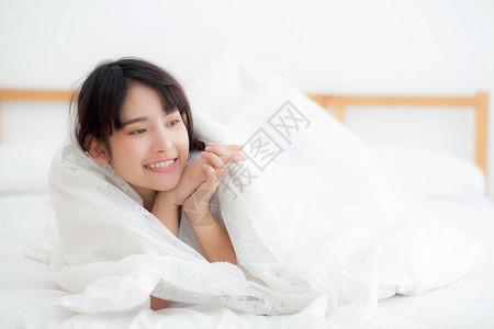 美丽的肖像年轻亚洲女人说谎和微笑早晨醒来时日出女孩在卧室里快乐的安得生活方式和放松概念图片
