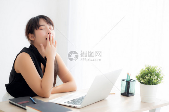 在办公室的笔记本电脑上工作无聊疲劳的年轻自由职业女在笔记本上懒睡和打哈欠的女孩精疲力尽的女秘书商业概念图片
