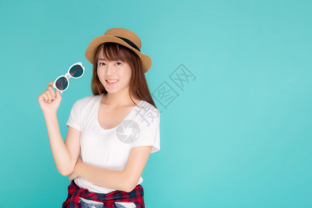 年轻女戴着帽子拿太阳镜微笑地表达自信享受夏天的假期远离蓝背景女孩快乐地穿戴时装旅行概念图片