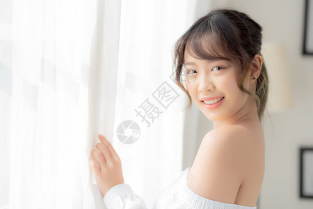 美丽的年轻亚洲女站在窗户边微笑早上醒来时日出女孩对新鲜欢乐生活方式和放松概念感到快乐图片
