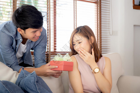 年轻的亚裔夫妇一起庆祝生日Asia男人送礼物盒给女惊喜在客厅女感到快乐和兴奋的周年纪念日假情人节的概念图片