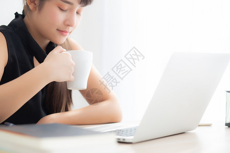 美丽的年轻自由职业女在书桌办公室微笑工作和用笔记本喝咖啡商业生活方式概念与专业女孩一起在笔记本办公室和电脑上微笑图片