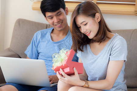 年轻的亚裔夫妇一起庆祝生日Asia男人送礼物盒给女惊喜在客厅女感到快乐和兴奋的周年纪念日假情人节的概念图片