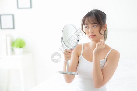 美丽的年轻女在卧室照镜子时面部美容有问题治疗图片