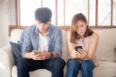 在沙发上坐着的年轻夫妇对关系有问题因为成瘾的社交网络媒体在一起图片