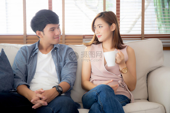 美丽的年轻夫妇笑着说故事坐在沙发上和女人一起喝咖啡男人和女放松享受生活方式的概念图片