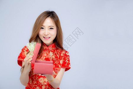 美丽的肖像年轻女青春服装微笑着带红色礼物盒在白背景上美丽的亚年女孩穿着qipao庆典令人兴奋快乐的新年假日概念图片