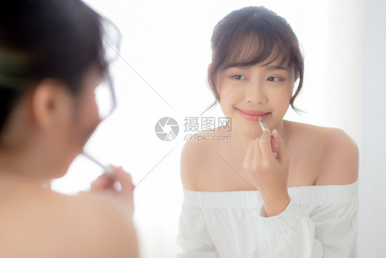 美丽的肖像年轻女看着镜子在房间里涂上化妆口红美唇容的女孩化妆和时尚在家里的口腔生活方式和保健概念图片