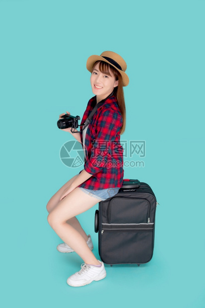 坐在行李上笑的年轻女乘暑假出国旅行快乐的Asia女孩拿着相机坐在手提箱上图片