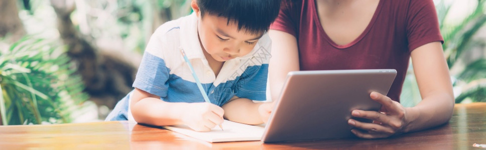 儿子使用数字平板电脑与母亲一起学习和上网家庭教育娱乐母亲教男孩和做家庭作业生活方式概念横幅网站图片
