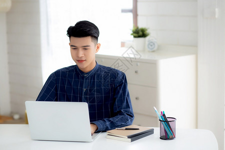 在家用笔记本电脑在办公桌上工作的年轻商人自由职业的男坐在家中使用笔记本进行交流和在桌上放松创业者在新的正常图片