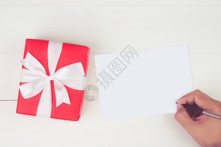 持空白贺卡写信件的人手在木制餐桌上有红色礼品盒现货和包装明信片模型顶视平地复制空间假日概念图片