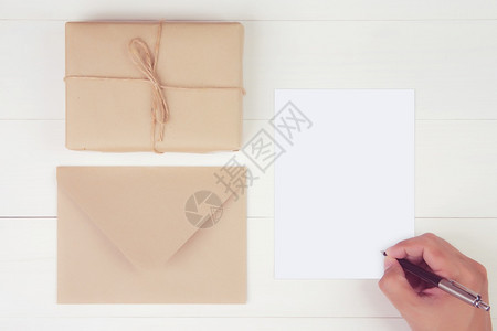 持空白贺卡写信件的人手持礼品盒木制桌子现货或包装纸明信片模型顶层视线平板复制空间假日概念上贴着Kraft纸图片